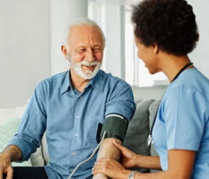 Smiling senior man having blood pressure checked by nurse during in-home health care appointment