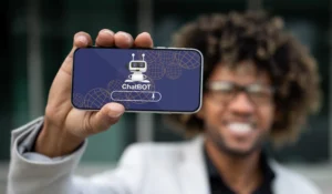 Smiling man holding a smartphone displaying a chatbot app interface, representing AI-driven support in home care services
