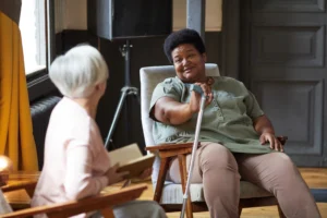 Elderly woman with a cane talking to a friend in a supportive home care setting