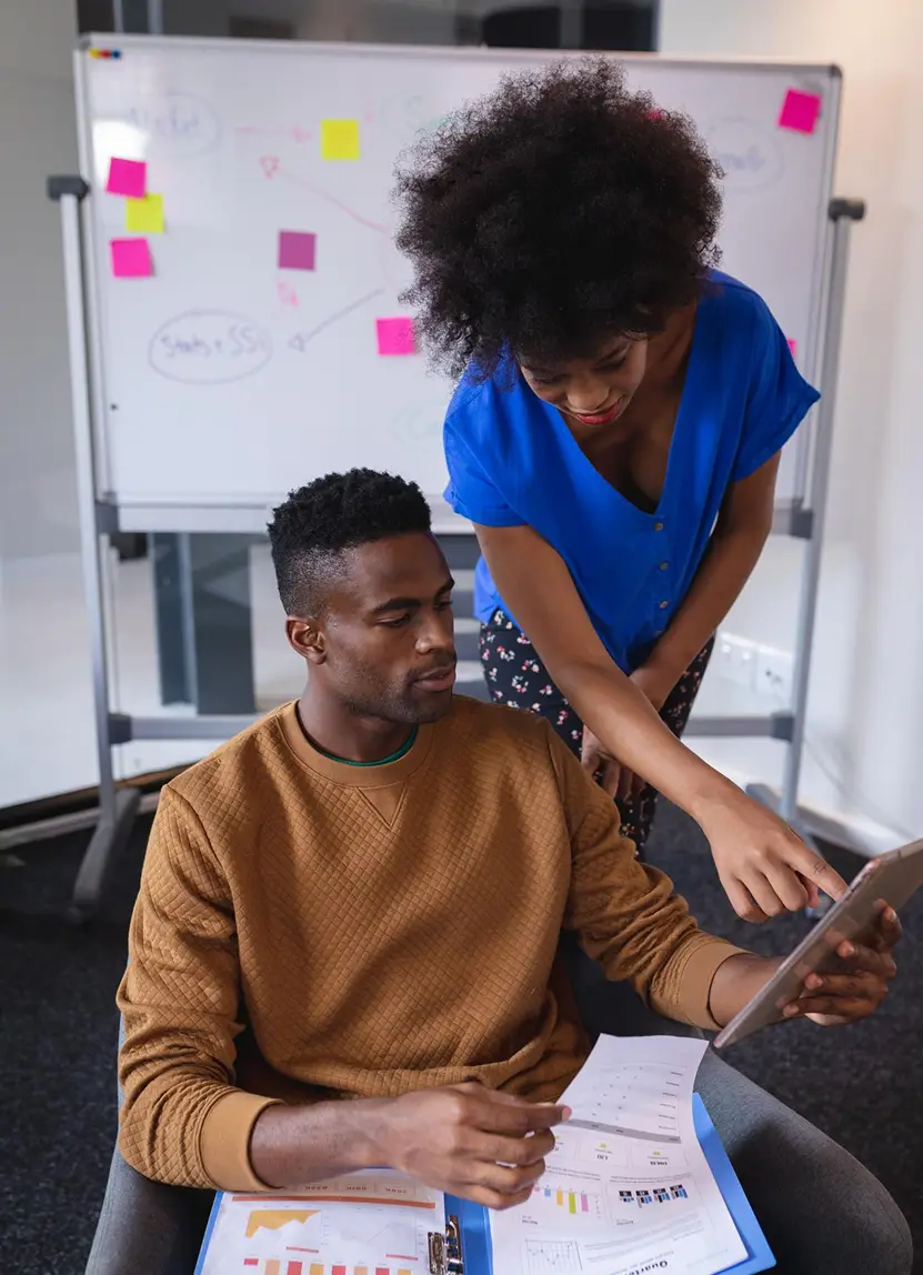 Two coworkers reviewing a tablet and documents in an office.