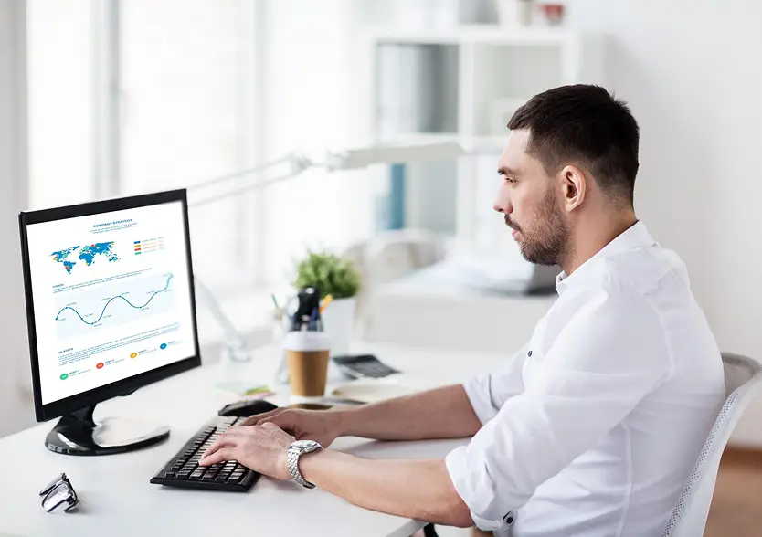 Man working at a desktop computer with charts on screen.