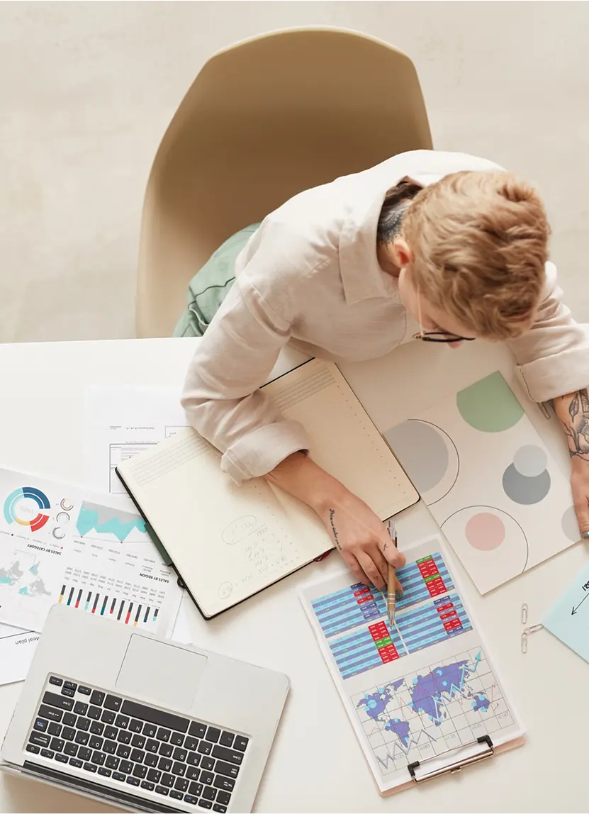Person analyzing charts and financial data at a desk with a laptop and notebook.