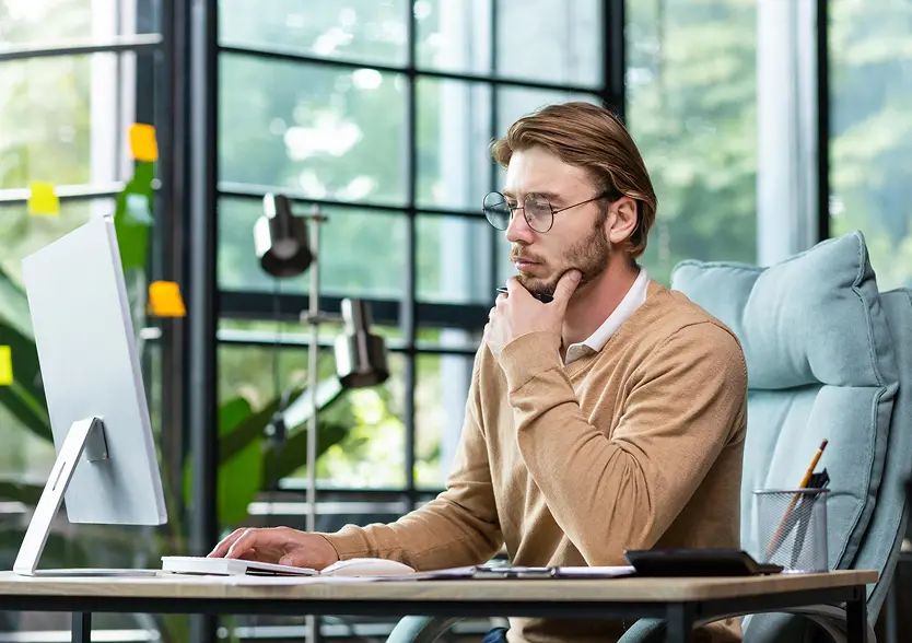 Man working at a computer desk, looking thoughtful and focused.