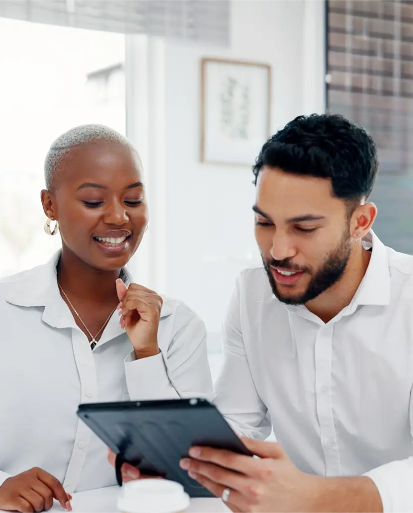 Two smiling colleagues in white shirts reviewing content on a tablet together in a bright office